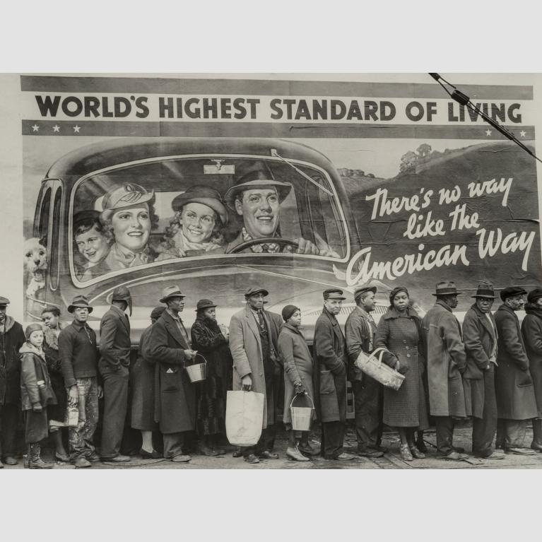 People stand in a line, some holding baskets, bags, or pails, in front of a billboard.